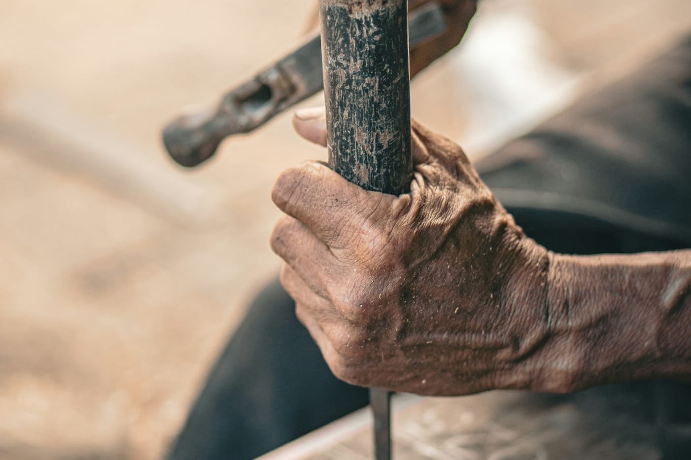 Weathered hands working a hammer and chisel against a slab of stone.