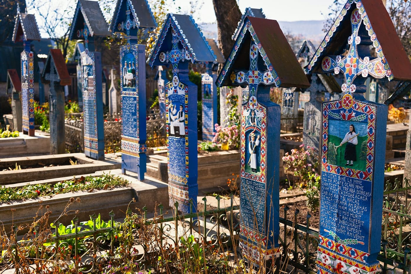 Blue painted wooden crosses in Săpânța, Romania, each with a small painted portrait and lines of verse.