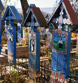 Blue painted wooden crosses in Săpânța, Romania, each with a small painted portrait and lines of verse.