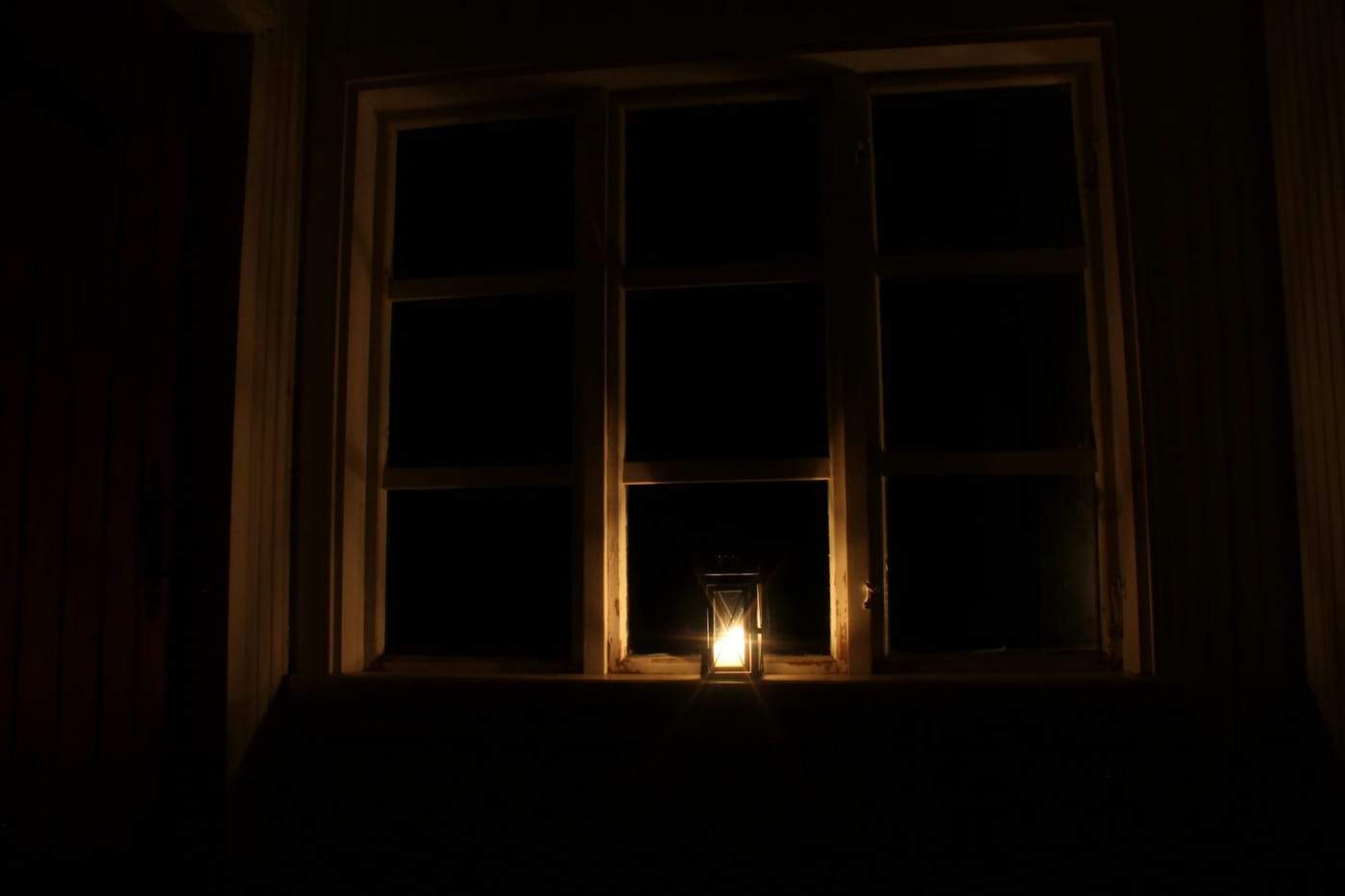 A single lit candle glowing at the bottom of a dark window at night.